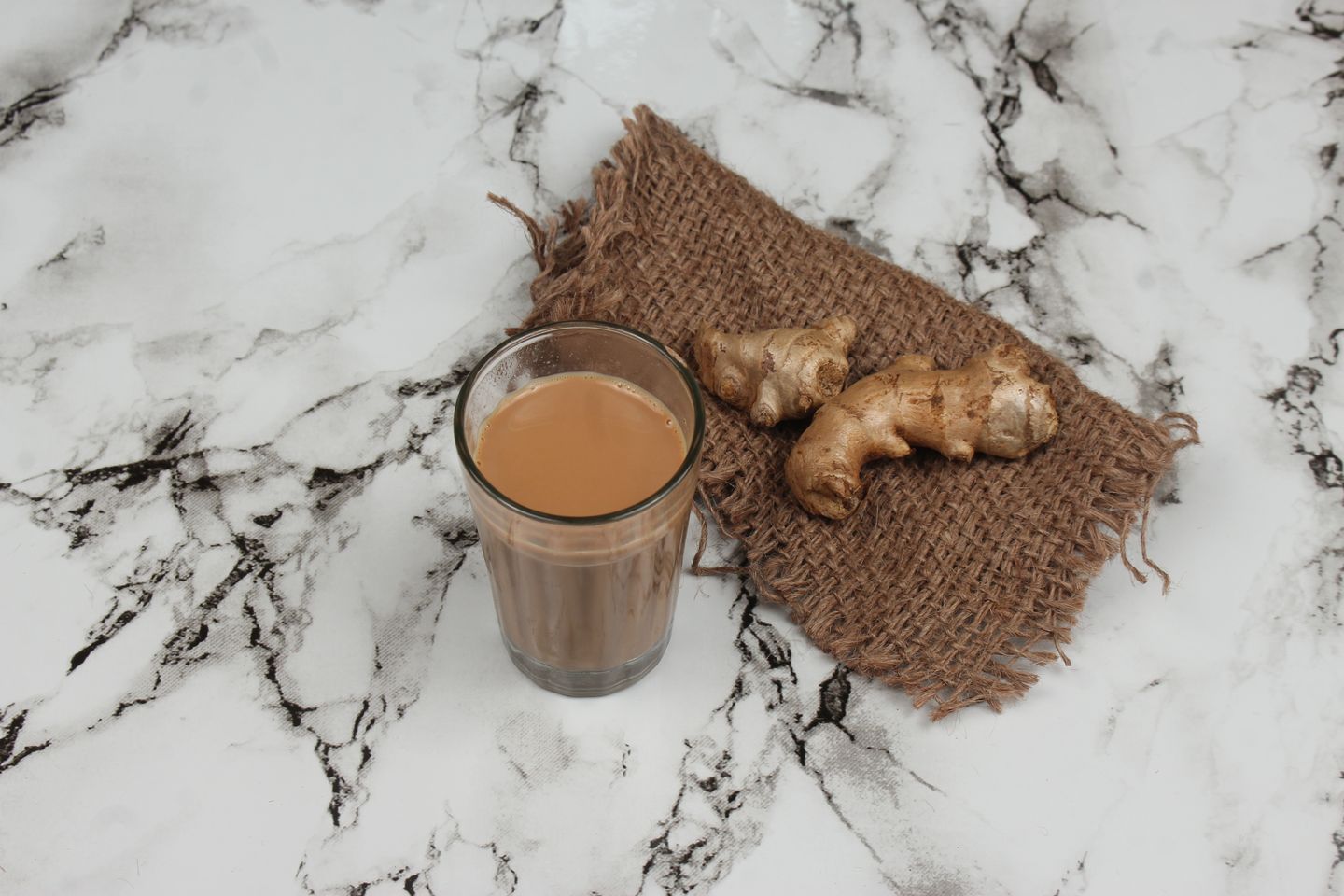 Indian milk tea in a glass on a light marble table — illustrative food photography